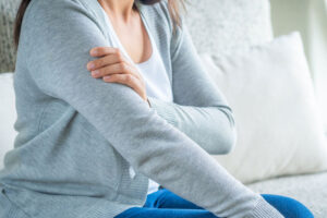 patient holding shoulder in pain while sitting on couch at home