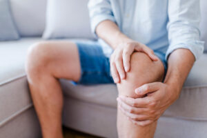 patient holding painful knee while sitting on couch