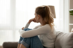 Woman sitting on a couch holding her knees, appearing to experience emotional or chronic pain