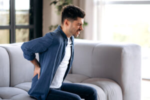 Man experiencing lower back pain from sciatica while sitting on couch