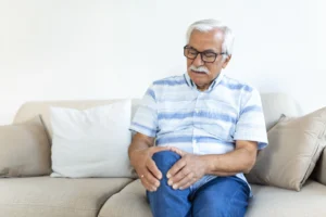 An old man is sitting a sofa holding his knee because of Joint Pain After Your Workout