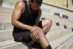 man is sitting and holding his knee as he is suffering form Knee Hyperextension