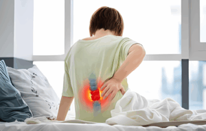 woman is sitting on her bed suffering from lower back pain