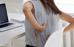 woman is seatong on her desk suffering from back pain