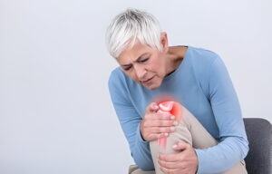 woman is seatin on chair and holding her leg as she is suffering from knee pain