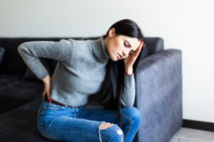 Young Woman suffering back ache and complaining sitting on a couch in the living room at home